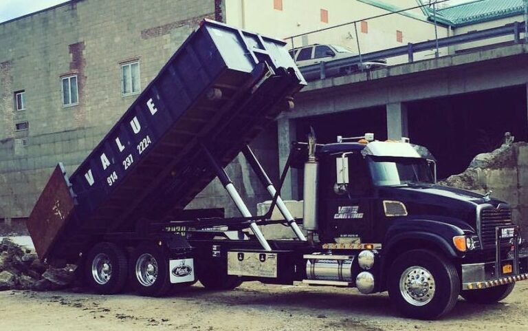 A black roll-off truck with the Value Carting logo, unloading a dumpster.