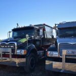 Two black roll-off trucks with the Value Waste logo, parked side-by-side.