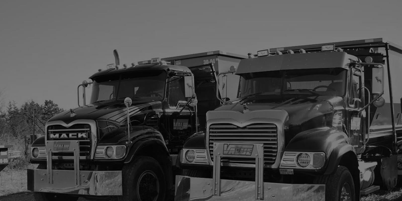 Two black roll-off trucks parked side-by-side, in a black and white image.