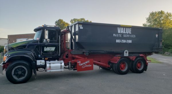 A black roll-off truck with the Value Waste logo, parked on a street.