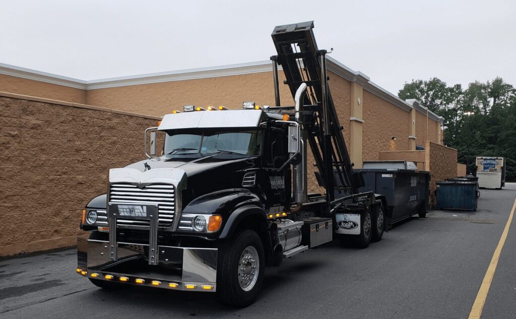 A black roll-off truck with the Value Waste logo, parked in front of a store.