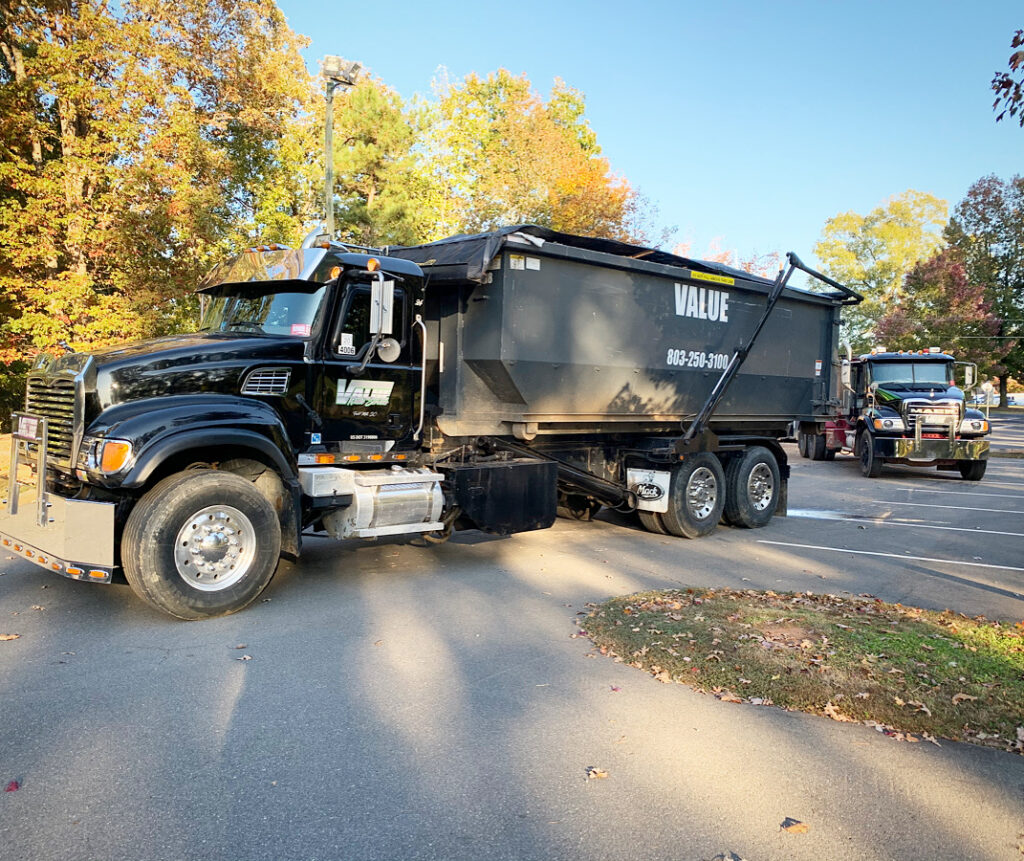 A black roll-off truck with the Value Waste logo parked in a parking lot.
