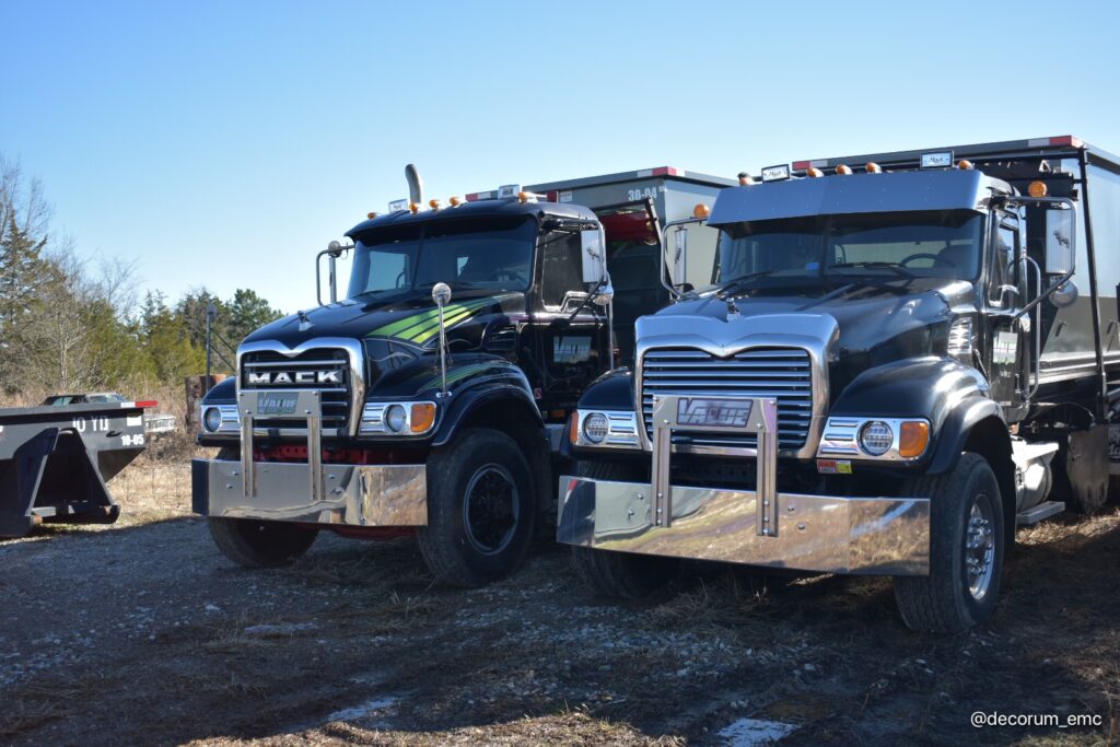 Two black roll-off trucks with the Value Waste logo, parked side-by-side.
