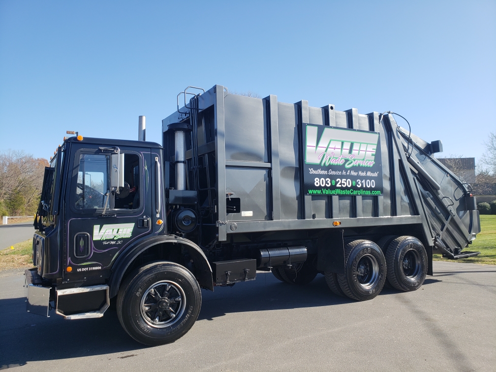 A black garbage truck with the Value Waste logo, parked on a street.