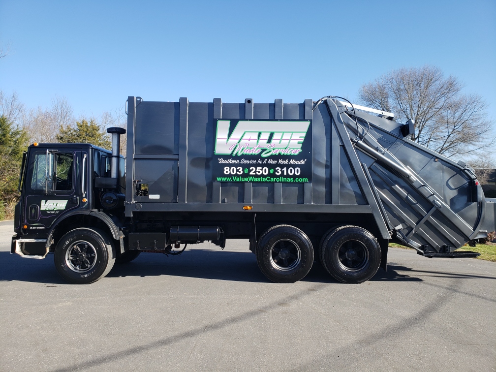 A black garbage truck with the Value Waste logo parked on a street.