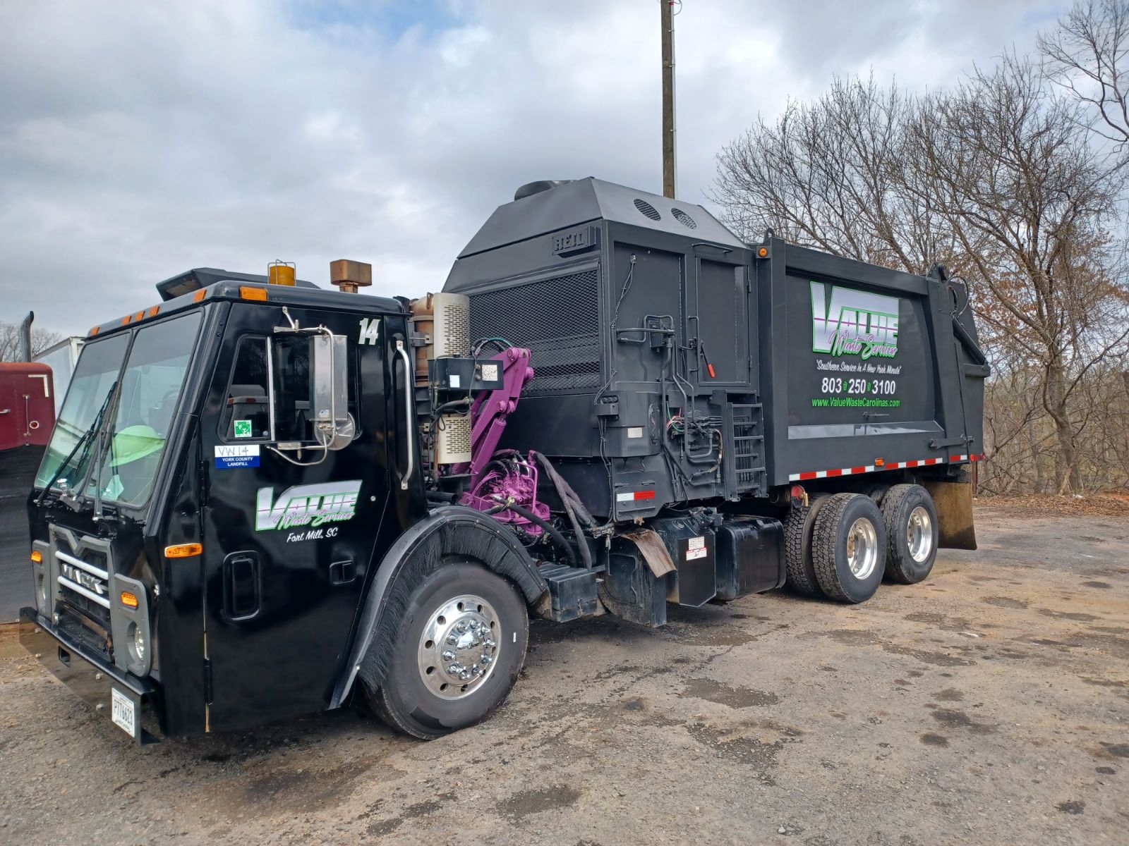 A black garbage truck with the Value Waste logo, parked in a yard.