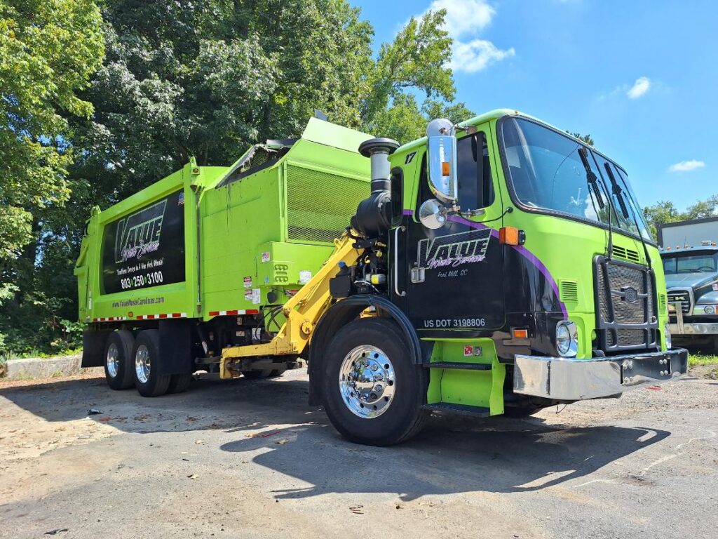 A green garbage truck with the Value Waste logo, parked on a street.